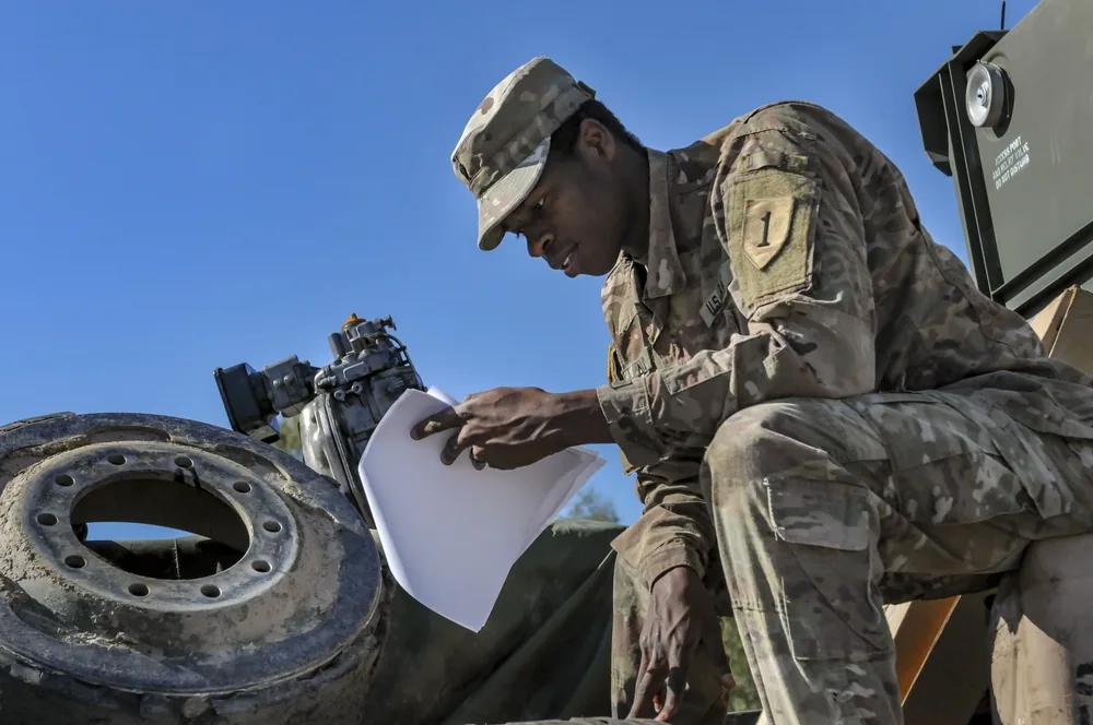 U.S. Army soldier checking supply paperwork beside equipment and mechanical parts